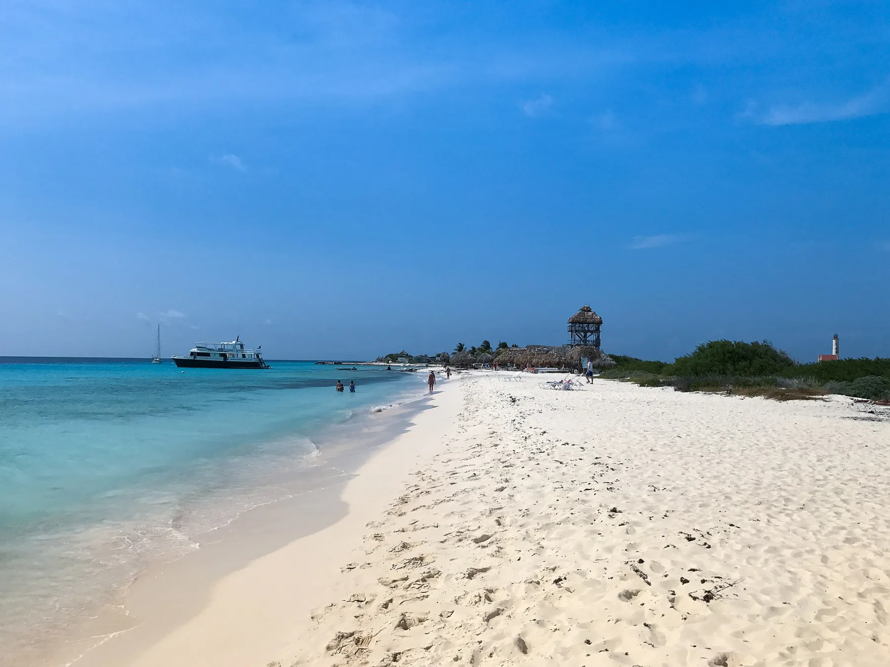 Spierwit strand van Klein Curaçao met turquoise ondiepe zee en de vuurtoren zichtbaar in de verte